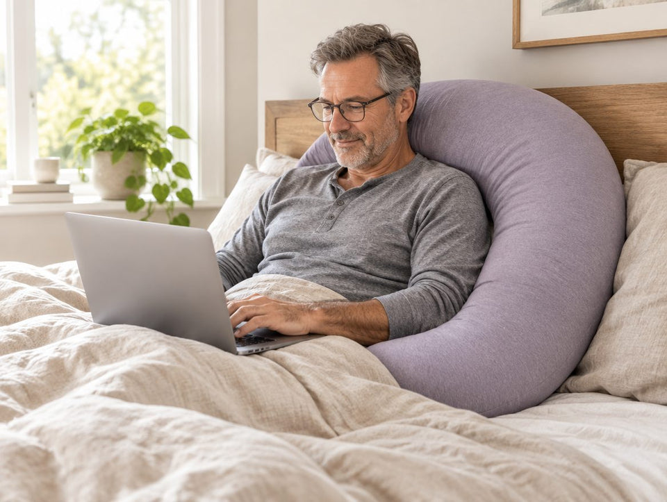 Man reading, propped up in bed against the pillow